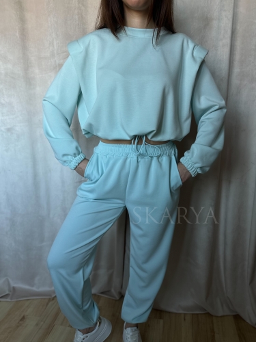 Niebieski komplet dresowy damski. Bluza typu crop regulowana ściągaczem, z poduszkami na ramionach. Spodnie typu jogger ze ściągaczem na nogawkach. Nietypowy dres, który łączy w sobie wygodę i modowy charakter. Wykonany z miękkiego w dotyku materiału.