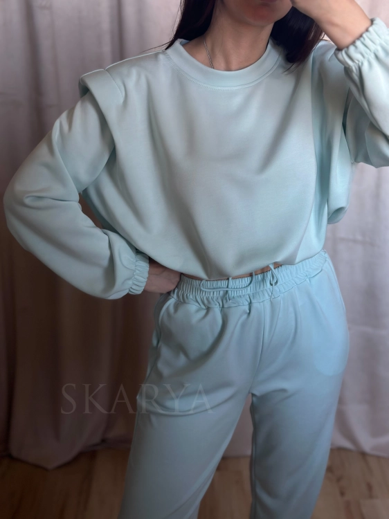 Niebieski komplet dresowy damski. Bluza typu crop regulowana ściągaczem, z poduszkami na ramionach. Spodnie typu jogger ze ściągaczem na nogawkach. Nietypowy dres, który łączy w sobie wygodę i modowy charakter. Wykonany z miękkiego w dotyku materiału.