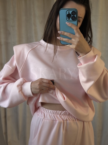 dresowy komplet damski w odcieniu pudrowego różu, składający się z bluzy, która posiada poduszki na ramionach i ściągacze u dołu bluzy i na rękawach oraz spodni na gumce z szeroką nogawką wide leg